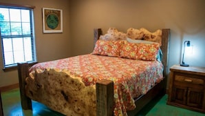 A bed with a floral bedspread, a wooden headboard, a nightstand with a lamp, and a window with blinds. - Riverfront Cabins  and  Vacation Homes (Rio Frio)
