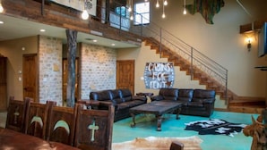 A spacious living area with a large couch, a dining table with chairs, a staircase, and a stone wall. - Riverfront Cabins  and  Vacation Homes (Rio Frio)