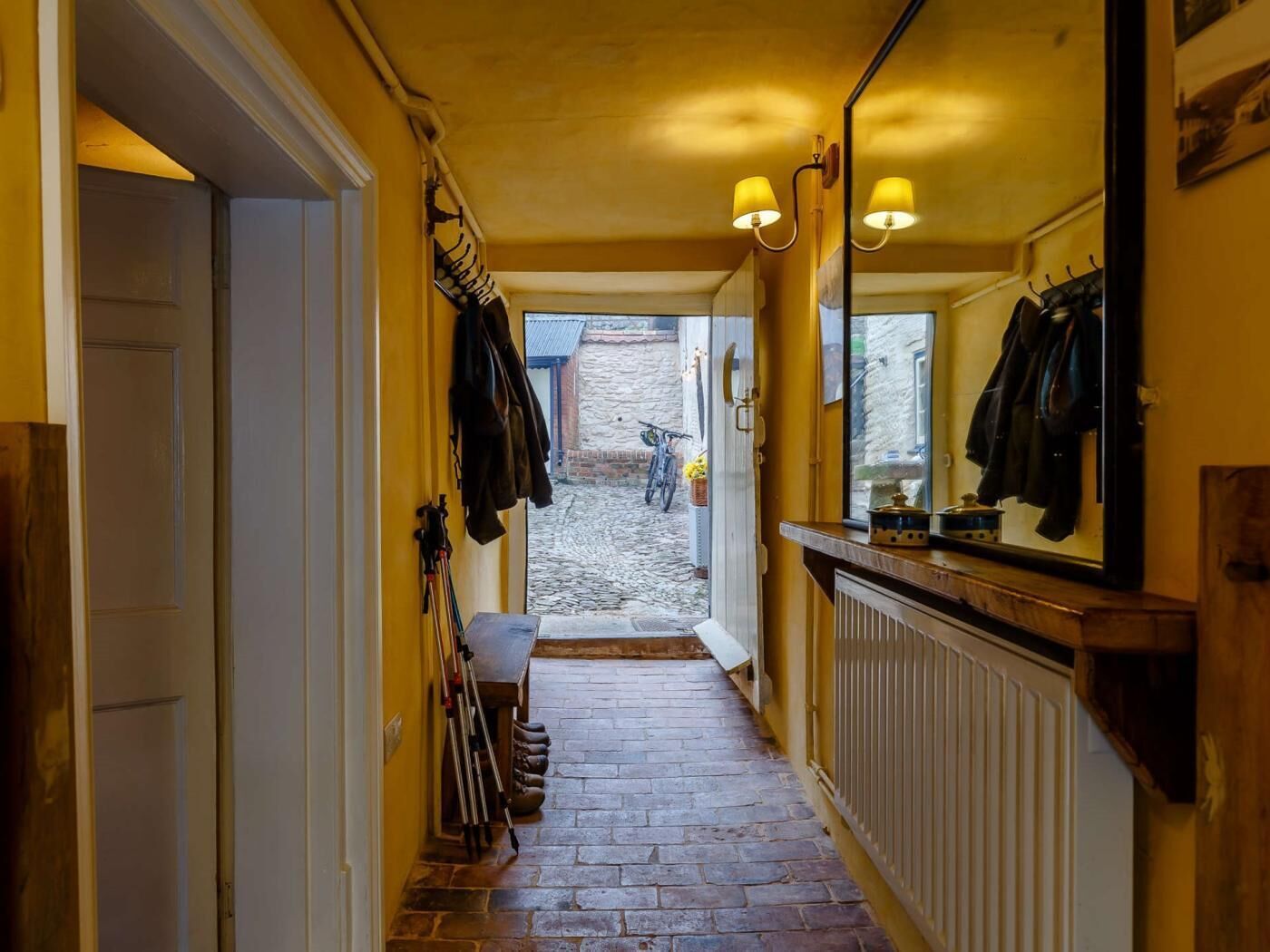 A narrow hallway with a stone floor, a wooden bench, and a mirror on the wall.