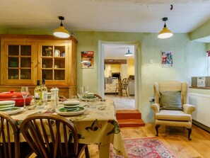 A dining area with a table set for four, a wooden cabinet with glass doors, and a chair with a cushion. - 4 Bed in Minehead (oc-90504) (Dunster)