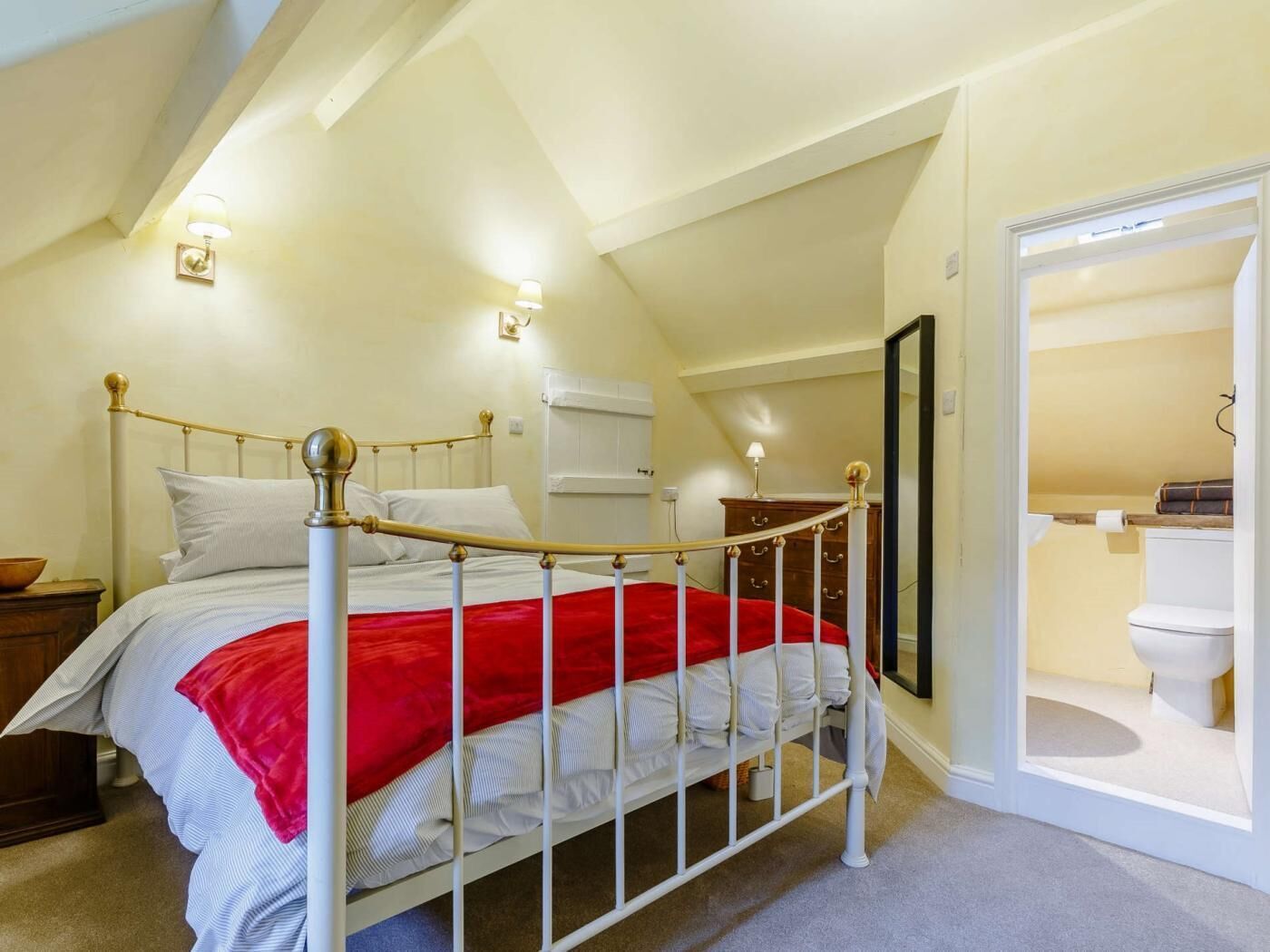A bedroom with a bed, a wooden nightstand, a dresser, and a bathroom visible through an open door.
