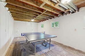 Een tafeltennistafel in een kamer met houten balken, witte muren en een ventilator.