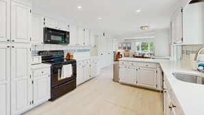 A modern kitchen with white cabinetry, a black stove, and a stainless steel sink. - West Falmouth Family Retreat Near Chapoquoit Beach (Falmouth)