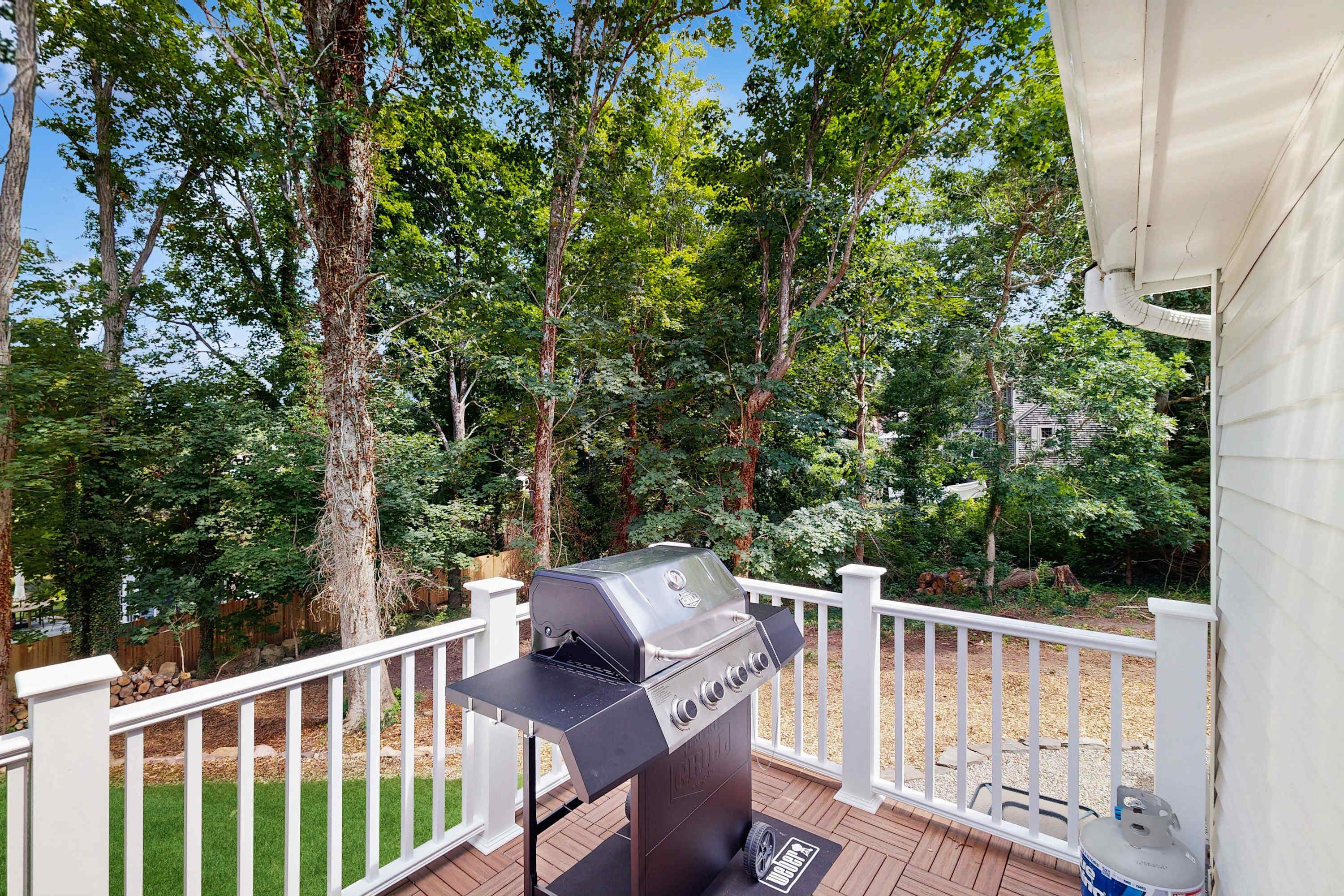 A deck with a barbecue grill, white railing, and trees in the background.