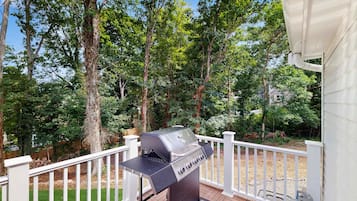 A deck with a barbecue grill, white railing, and trees in the background.