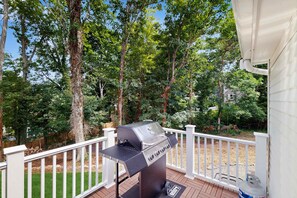 A deck with a barbecue grill, white railing, and trees in the background.