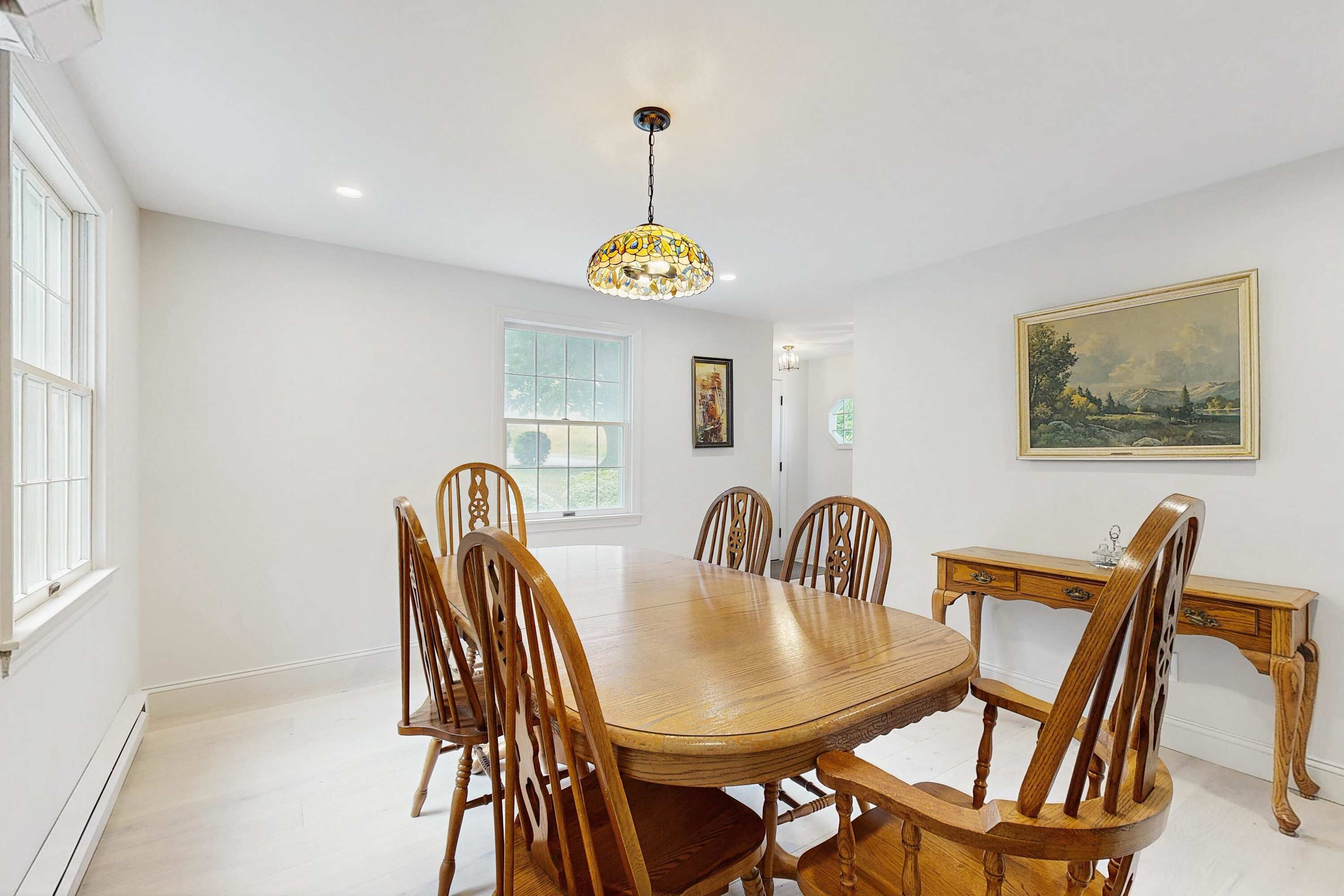A dining room with a wooden table and chairs, a chandelier, and a painting on the wall.