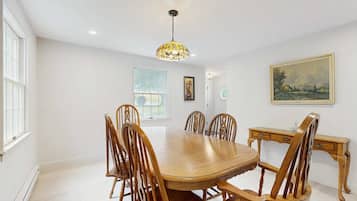 A dining room with a wooden table and chairs, a chandelier, and a painting on the wall.
