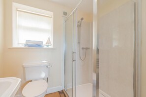 Ein Badezimmer mit Toilette, Duschkabine und einem Fenster über der Toilette.