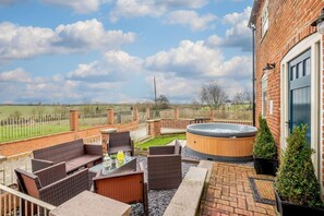 Eine Terrasse im Freien mit Korbmöbeln, einem Whirlpool und Blick auf die Landschaft.