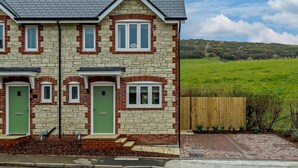A two-story house with a brick facade, green doors, and a fenced backyard. - 2 Bed in West Lulworth (oc-91197) (West Lulworth)