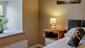 A hotel room with a bed, a bedside table with a lamp, a window with a curtain, a radiator, and a wall-mounted painting. - 3 Bed in Cosheston (oc-90732) (Cosheston)