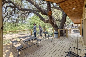 A wooden deck with picnic tables and chairs, surrounded by trees. - Riverfront Cabins  and  Vacation Homes (Rio Frio)