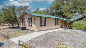 A single-story building with a green roof, a covered porch, and a gravel driveway. - Riverfront Cabins  and  Vacation Homes (Rio Frio)
