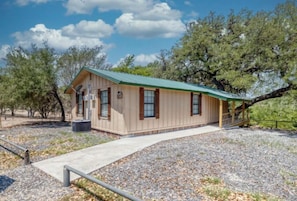 A single-story building with a green roof, a covered porch, and a gravel driveway. - Riverfront Cabins  and  Vacation Homes (Rio Frio)