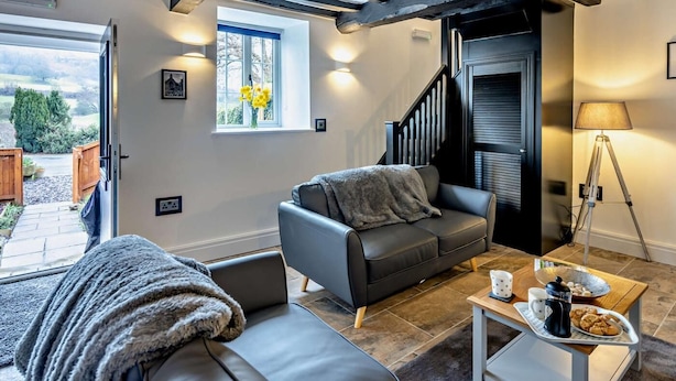 Ein modernes Wohnzimmer mit einer Couch, einem Couchtisch mit Frühstücksangeboten, einer Lampe und Blick ins Freie.