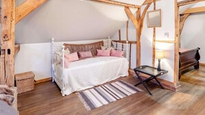 A bedroom with a wooden ceiling, a bed with white bedding and pink pillows, a bedside table with a lamp, and a striped rug. - 1 Bed in Billingshurst (oc-90733) (Loxwood)