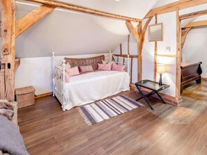 A bedroom with a wooden ceiling, a bed with white bedding and pink pillows, a bedside table with a lamp, and a striped rug. - 1 Bed in Billingshurst (oc-90733) (Loxwood)