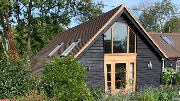A dark wooden house with a sloped roof, a large window, and a small door. - 1 Bed in Billingshurst (oc-90733) (Loxwood)