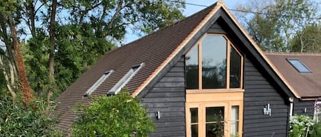 Una casa de madera oscura con techo inclinado, un ventanal grande y una puerta pequeña.