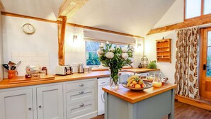 A kitchen with wooden cabinets, a fruit bowl, and a window with a view of trees. - 1 Bed in Billingshurst (oc-90733) (Loxwood)