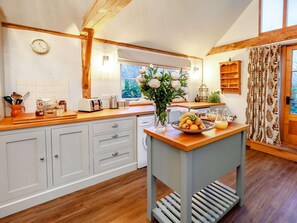 A kitchen with wooden cabinets, a fruit bowl, and a window with a view of trees. - 1 Bed in Billingshurst (oc-90733) (Loxwood)
