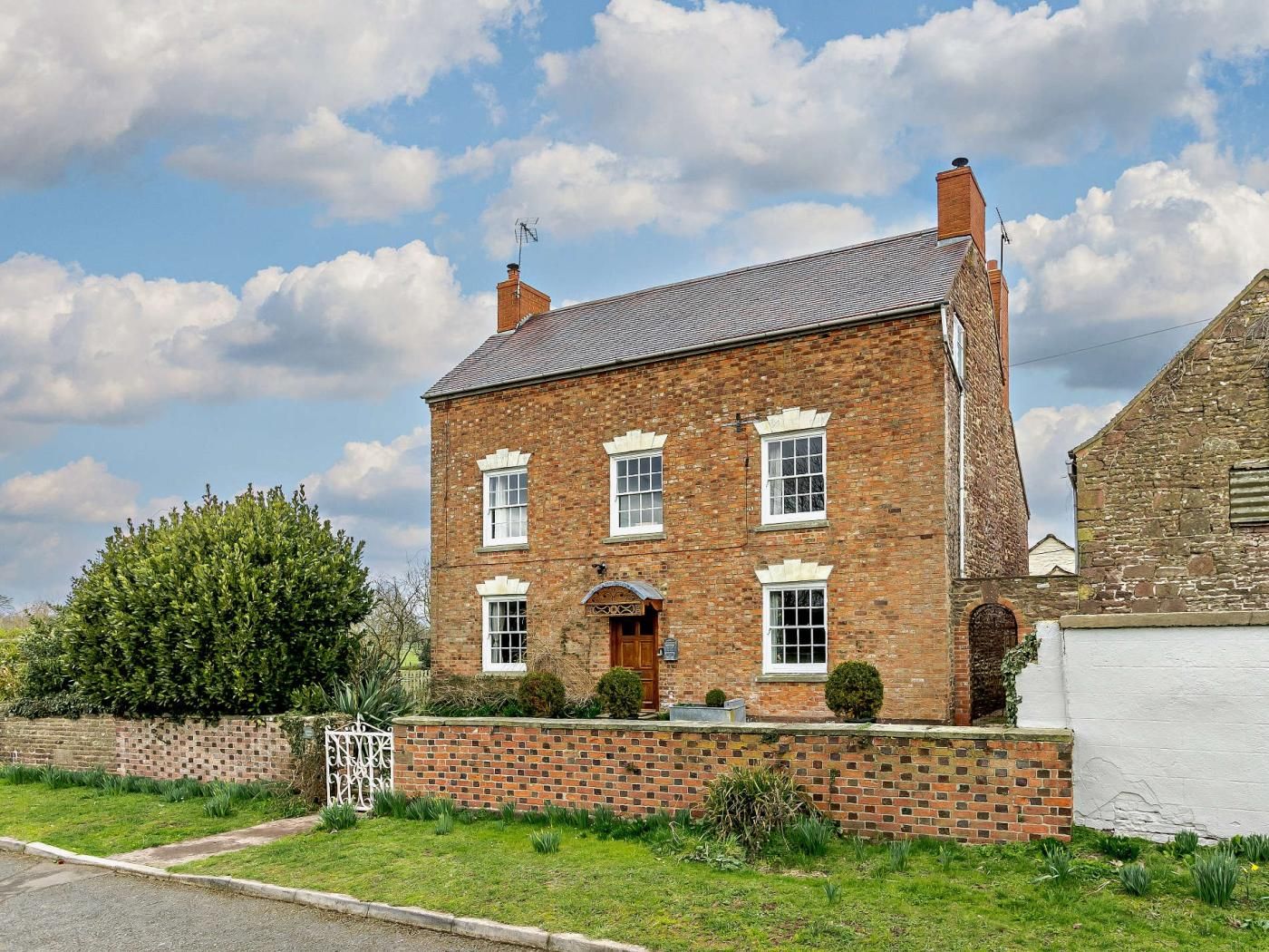A two-story brick house with a symmetrical facade, a central entrance, and a small front garden.