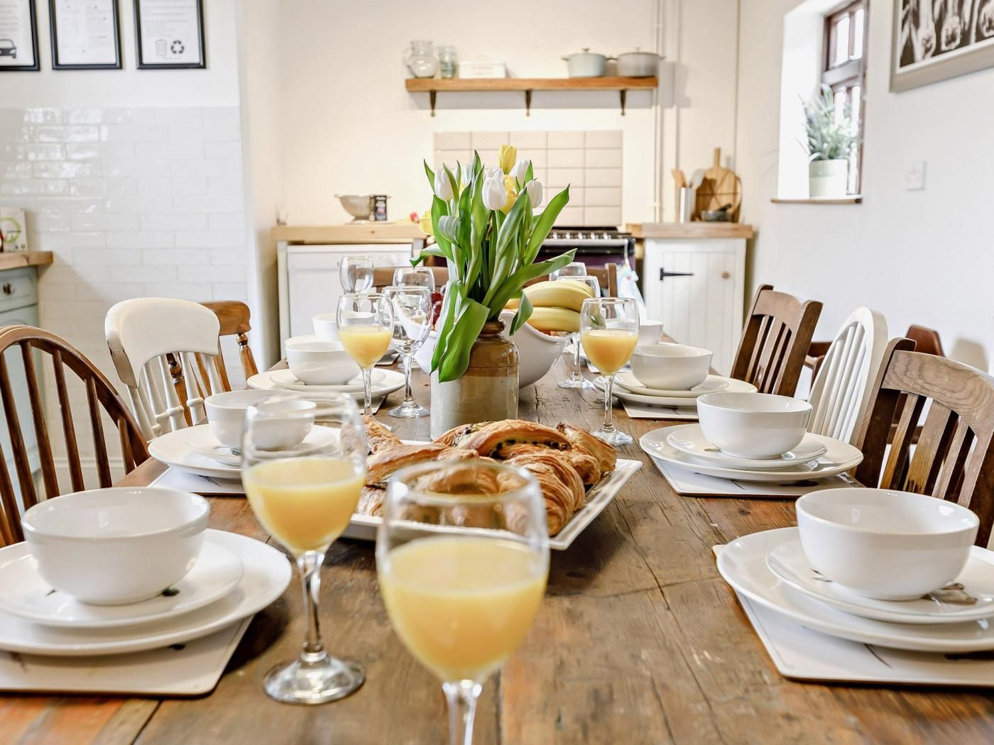 A dining table set with white plates, bowls, and glasses of orange juice, surrounded by wooden chairs.