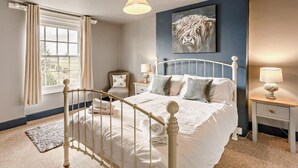 A bedroom with a bed, bedside tables, a lamp, a painting, and a window with curtains.
