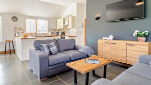Een moderne woonkamer met een grijze bank, een houten salontafel en een aan de muur bevestigde televisie.