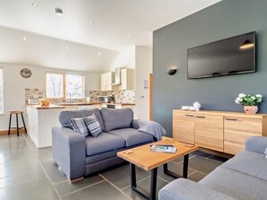 Ein modernes Wohnzimmer mit grauem Sofa, einem Holztisch und einem an der Wand befestigten Fernseher.