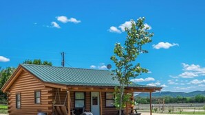 A wooden cabin with a porch, a small tree, and a clear sky. - Riverfront Cabins  and  Vacation Homes (Rio Frio)