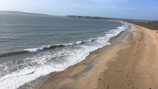 Ein Strand mit Wellen, blauem Himmel und fernen Klippen.