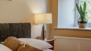 Ein ordentlich bezogenes Bett mit aufgerollten Handtüchern, einer Nachttischlampe, einer Topfpflanze und einer Heizung.