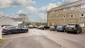 Ein Parkplatz mit mehreren Autos, ein Steinhaus mit vielen Fenstern und einem klaren Himmel.