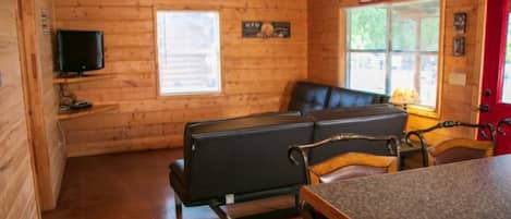 A wooden cabin interior with a sofa, chairs, a TV, and a window.