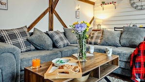 A cozy living room with a wooden ceiling, grey sofas, a coffee table with breakfast items, and a wall clock. - 1 Bed in Northwich (oc-91435) (Northwich)