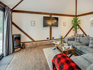 A cozy living room with a fireplace, a grey sofa, a flat-screen TV, and a wooden ceiling structure. - 1 Bed in Northwich (oc-91435) (Northwich)