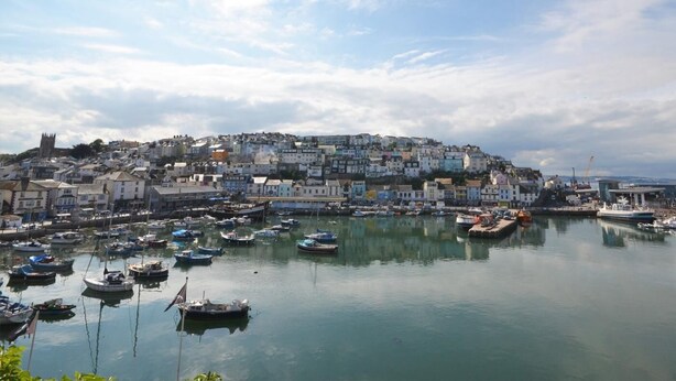 A coastal town with a harbor filled with boats, historic buildings, and a prominent church on a hill. - 2 Bed in Brixham (oc-91427) (Brixham)