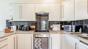 A modern kitchen with white cabinets, a black tiled backsplash, a built-in oven, a microwave, and a toaster. - 2 Bed in Brixham (oc-91427) (Brixham)