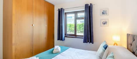 Un dormitorio con cama, armario, ventana con cortinas y lámpara.