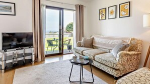 A living room with a TV, sofa, and a sliding glass door to the outside. - 2 Bed in Brixham (oc-91427) (Brixham)