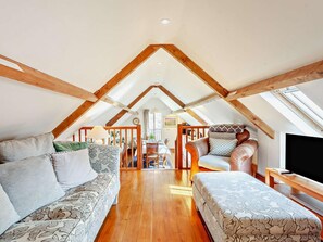 A cozy attic room with wooden beams, a sofa, a chair, and a TV. - 2 Bed in Malmesbury (oc-91453) (Malmesbury)