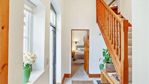 Ein Flur mit einer Holztreppe, einem Bett im Hintergrund und einer Zimmerpflanze rechts.