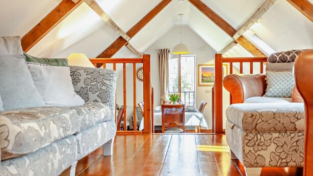 Ein Dachzimmer mit Holzbalken, zwei gemusterten Sofas, einem Esstisch und Blick ins Freie.
