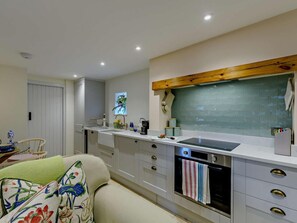 A modern kitchen with a built-in oven, a wooden beam above the countertop, and a dining area with a chair and table. - 1 Bed in Hawick (oc-91437) (Denholm)