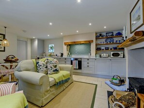 A cozy living room with a sofa, a small table, and a kitchen area with cabinets and a microwave. - 1 Bed in Hawick (oc-91437) (Denholm)