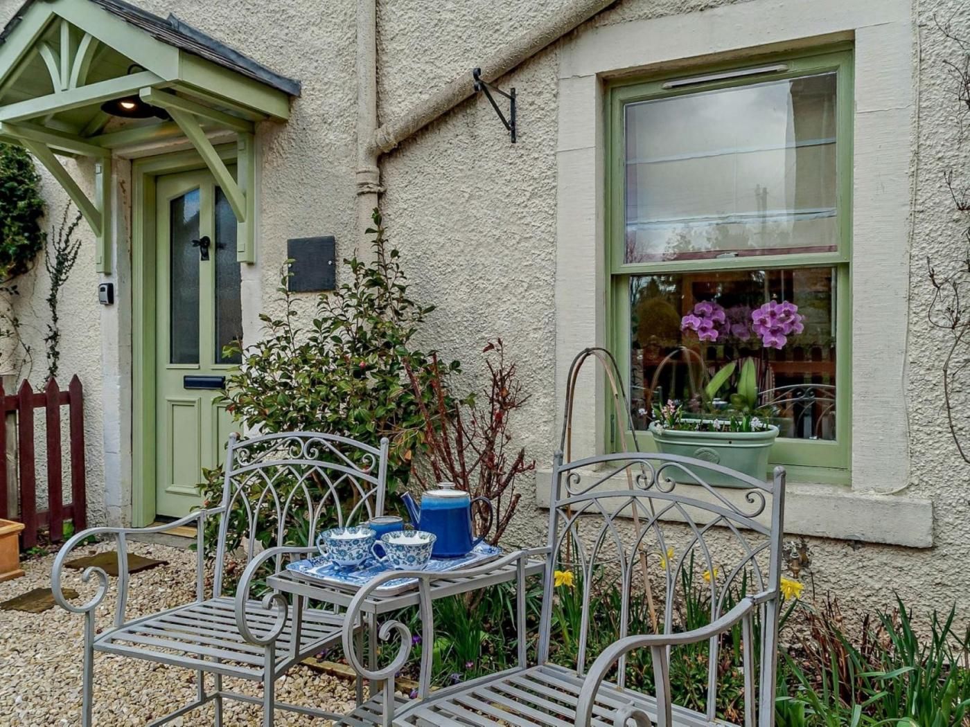 A metal bench with a table, a green door, and a window with flowers.