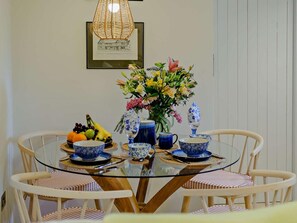 A dining area with a glass table surrounded by chairs, a vase with flowers, and a framed drawing on the wall. - 1 Bed in Hawick (oc-91437) (Denholm)