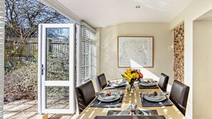 Un coin repas avec une table dressée pour six personnes, un vase de fleurs et une carte accrochée au mur.